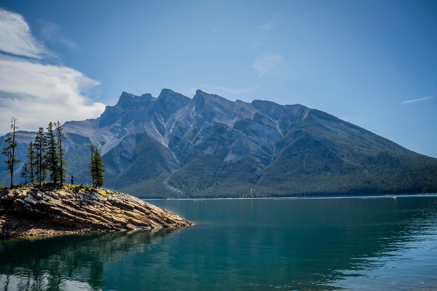 Scenic view of Lake Minnewanka with Mount Girouard towering in the background and evergreen trees on rocky shoreline.