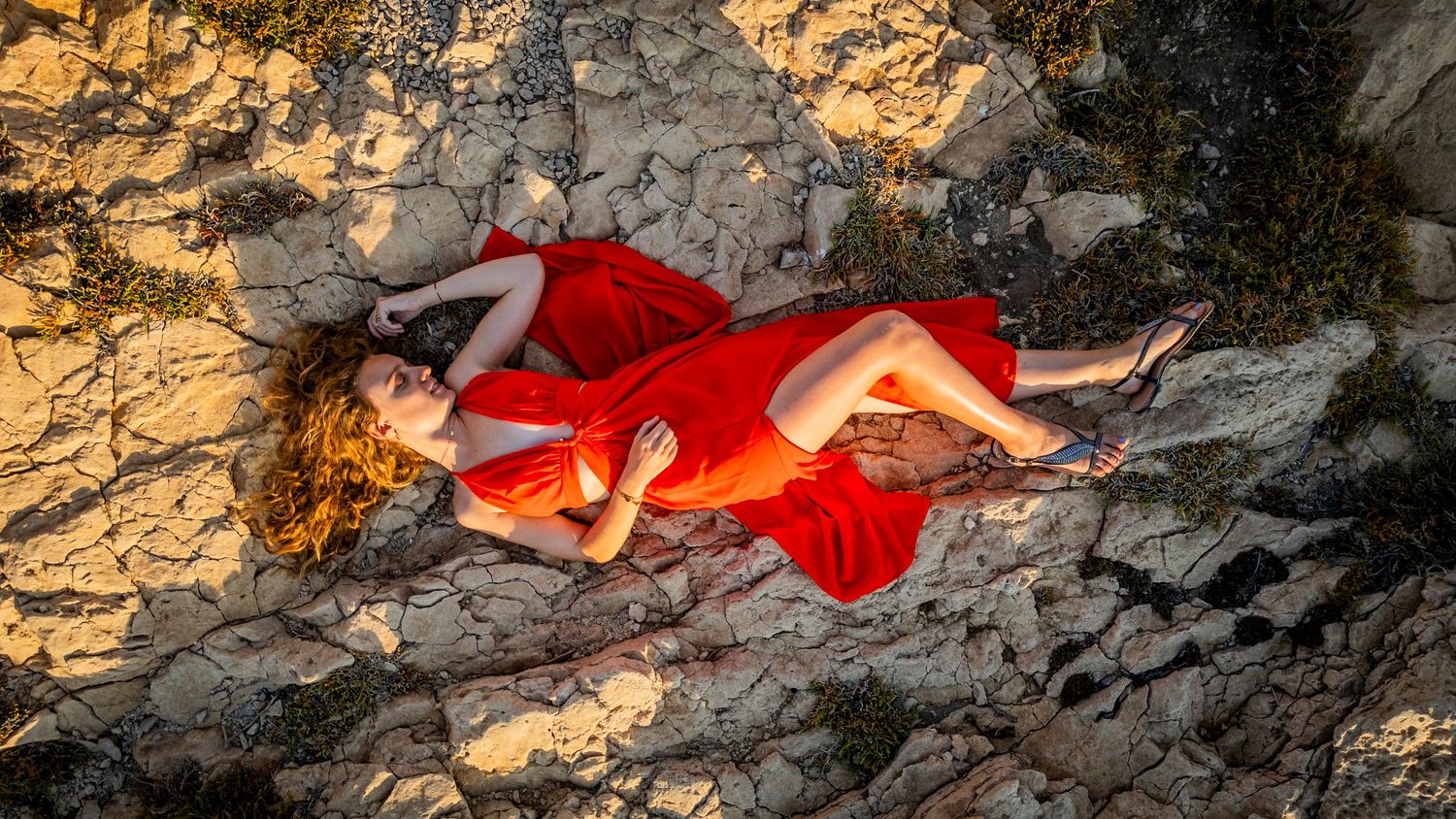 A red scarf trails artistically across rough gray rocks in a dramatic nature photography composition at sunset.