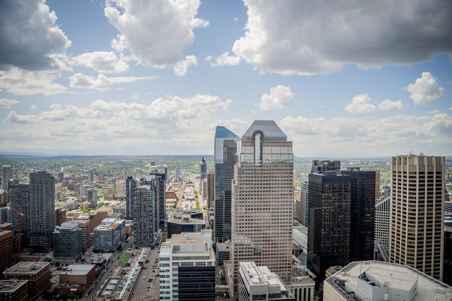 Panoramic aerial view of downtown Calgary's modern skyline with glass skyscrapers under dramatic cloudy skies.