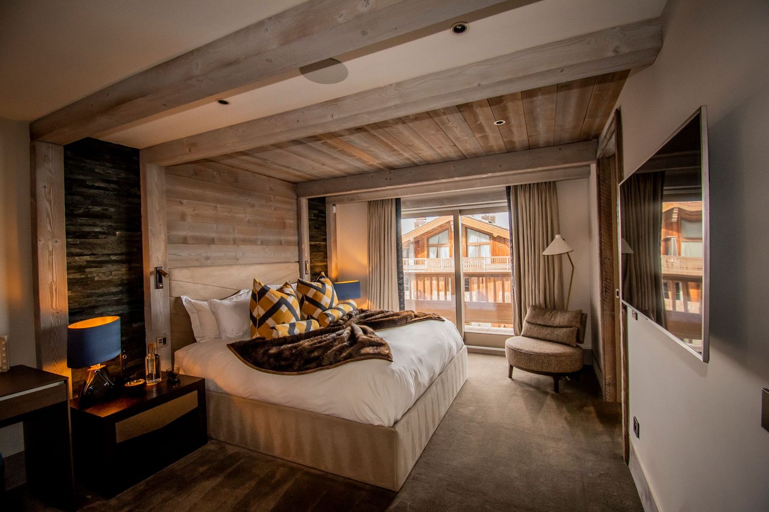 Luxurious mountain chalet bedroom with plush bedding, wood paneled walls, and scenic balcony views.