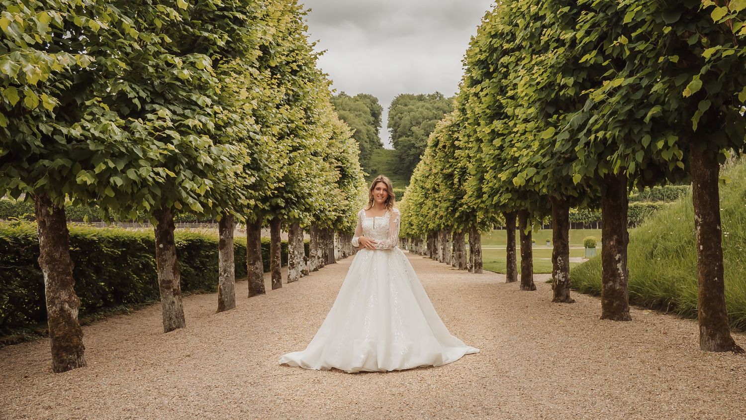 A panoramic view of a formal garden path lined with manicured trees and hedges leading to a grand estate.