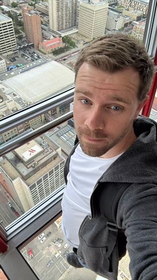 Aerial selfie taken from high up in a skyscraper looking down at city buildings and streets below through a window.