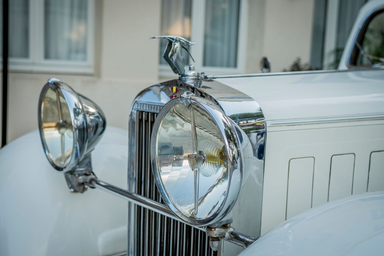 Classic black Rolls Royce vehicle hood ornament Spirit of Ecstasy sculpture against blurred urban background.