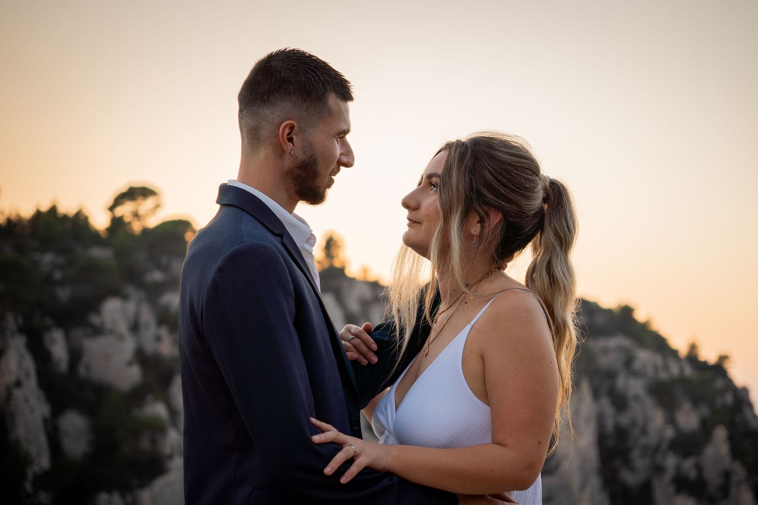 A romantic couple shares an intimate moment at sunset against a backdrop of steep cliffs.