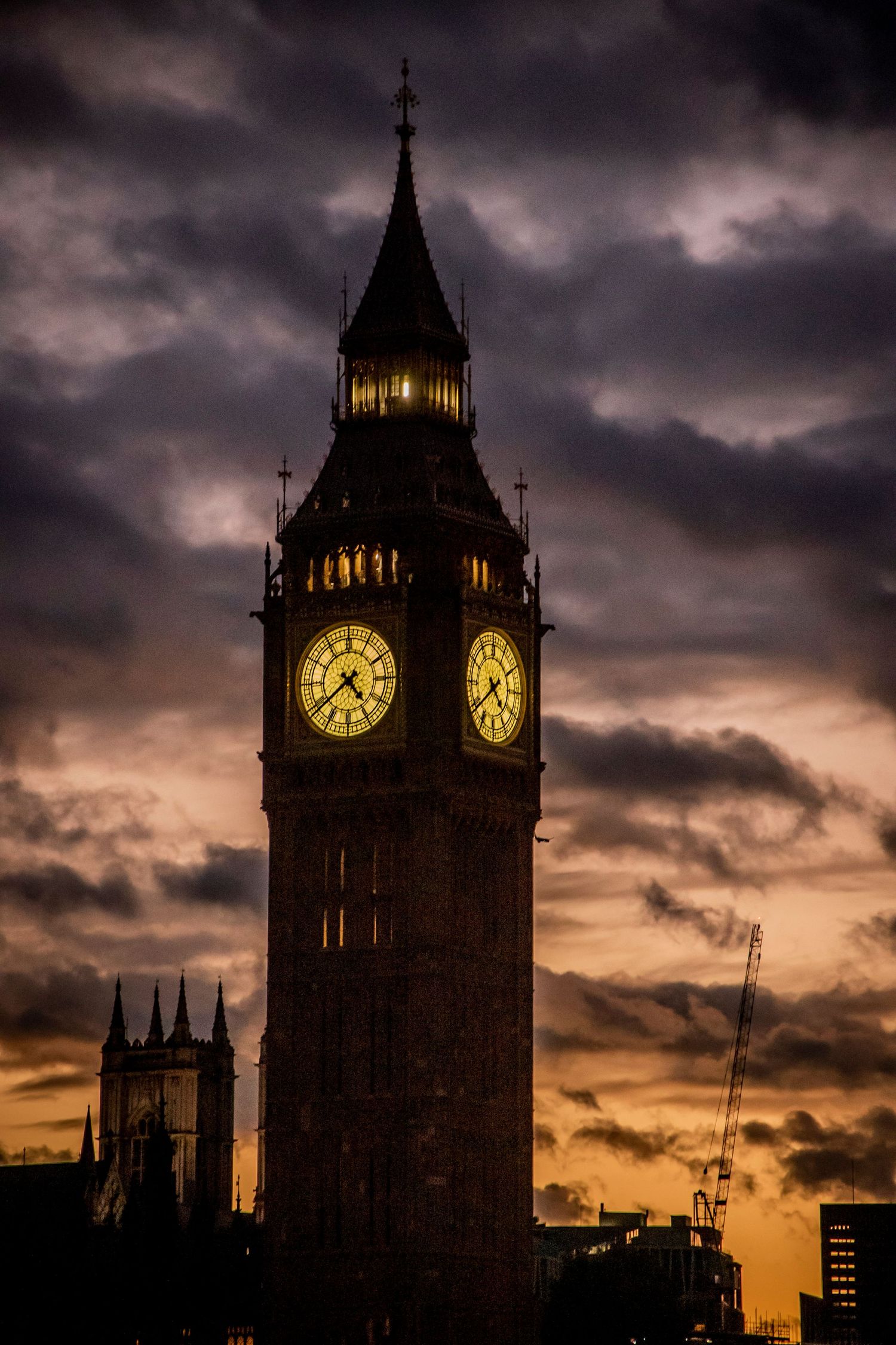 The iconic Big Ben clock tower silhouetted against a dramatic sunset sky with glowing orange clouds in London.