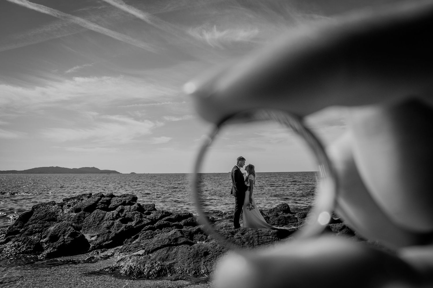 A creative black and white wedding photograph showing silhouettes through a lens with a rocky beach background.