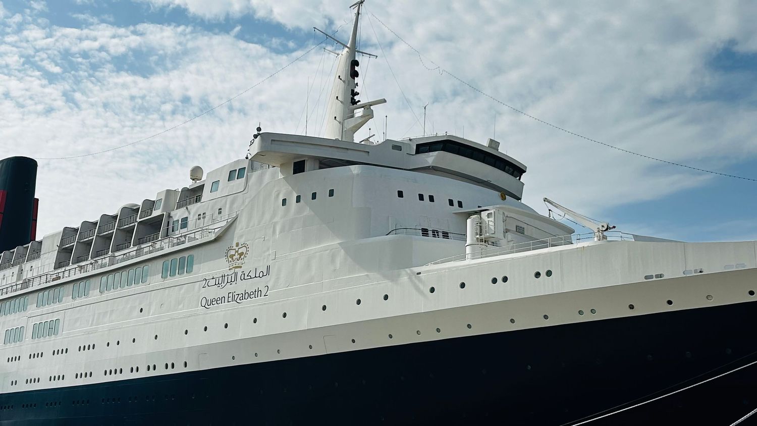 Large white and black passenger cruise ship with classic ocean liner design docked under cloudy sky.