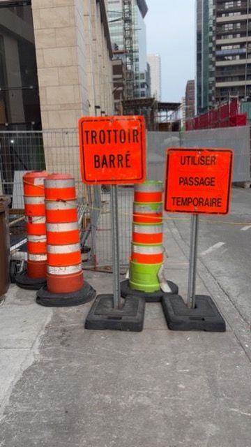 Orange construction signs in French with reflective barrels mark a temporary passage on an urban street construction site.
