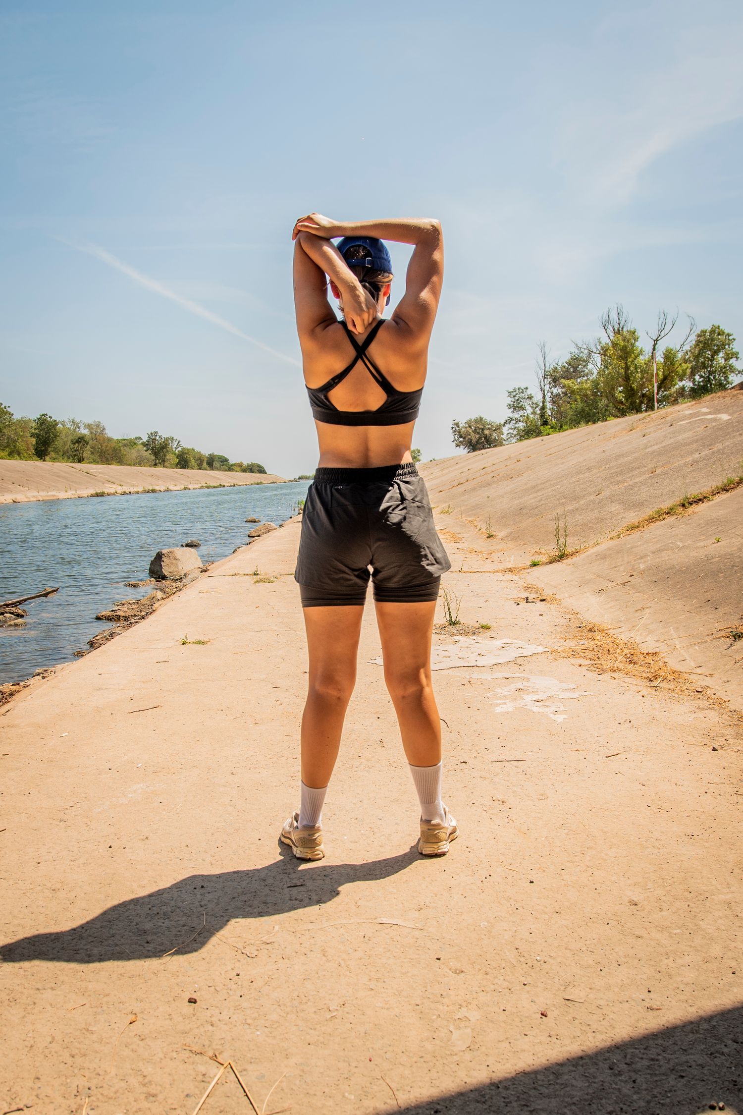 Athletic person stretching by a lakeside in workout attire on a sunny summer day.