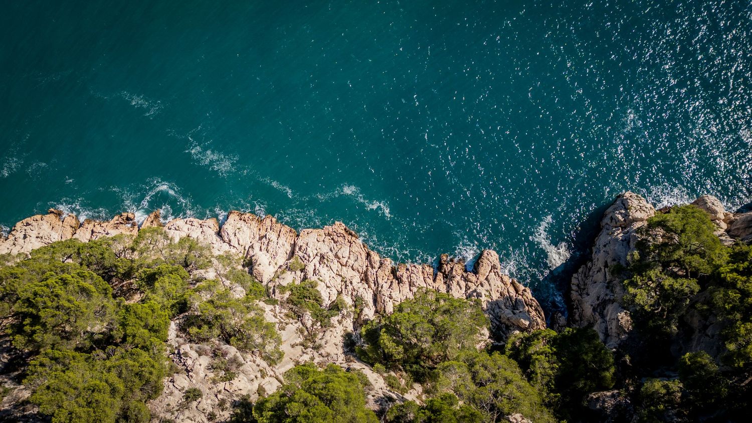 Aerial view of rugged Mediterranean coastline with steep rocky cliffs and turquoise blue waters below.