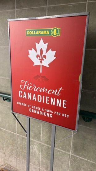 A Dollarama store sign displays a red poster featuring a maple leaf with fleur-de-lis design for 'Fièrement Canadienne' branding.