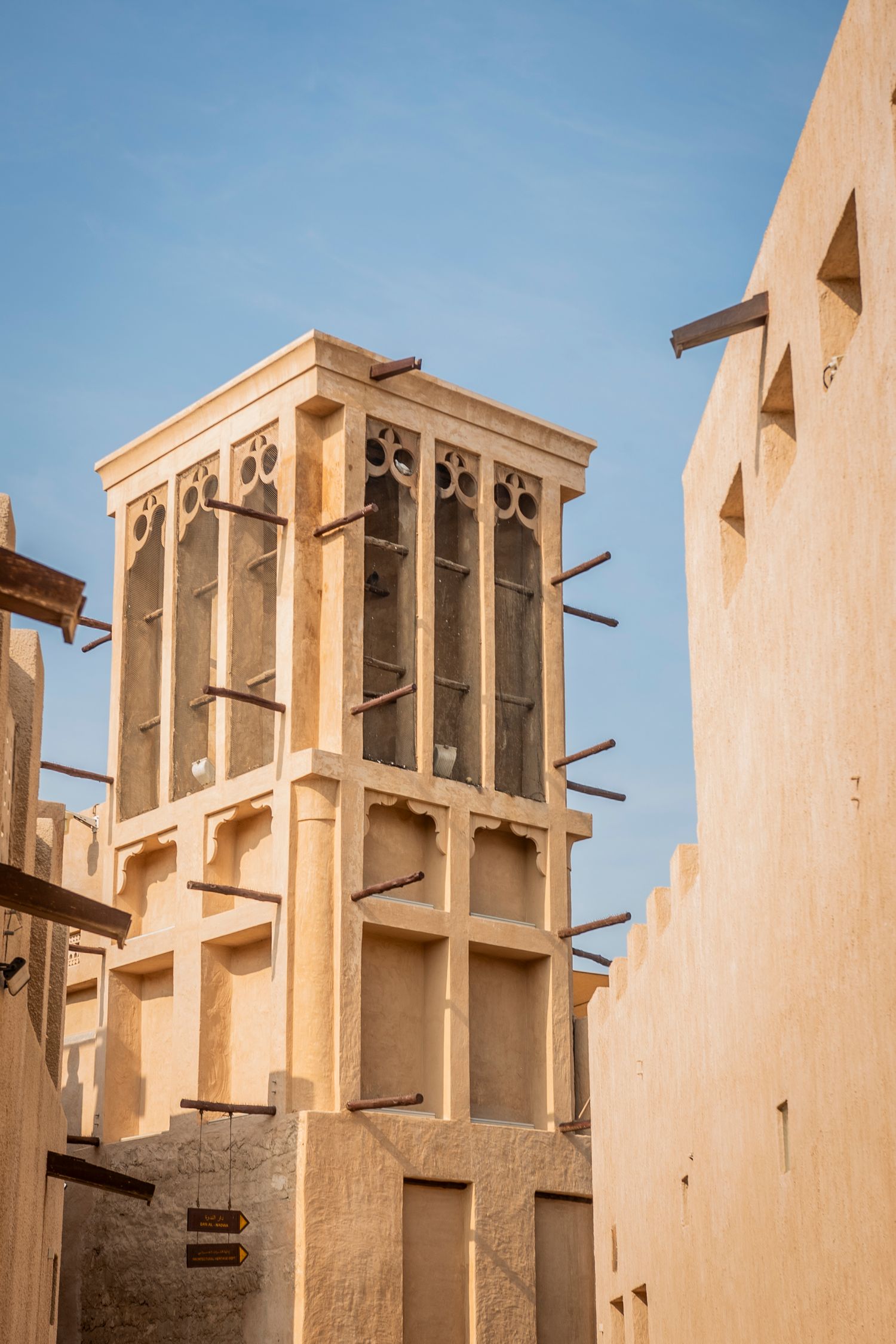 Traditional wind tower and ornate architecture of a historic building in Dubai's Al Bastakiya district against blue sky.