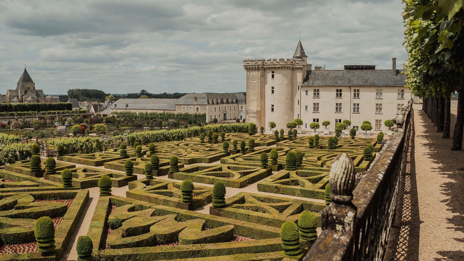 Ornate geometric garden maze with topiary hedges and white castle tower at Villandry Castle in Loire Valley, France.