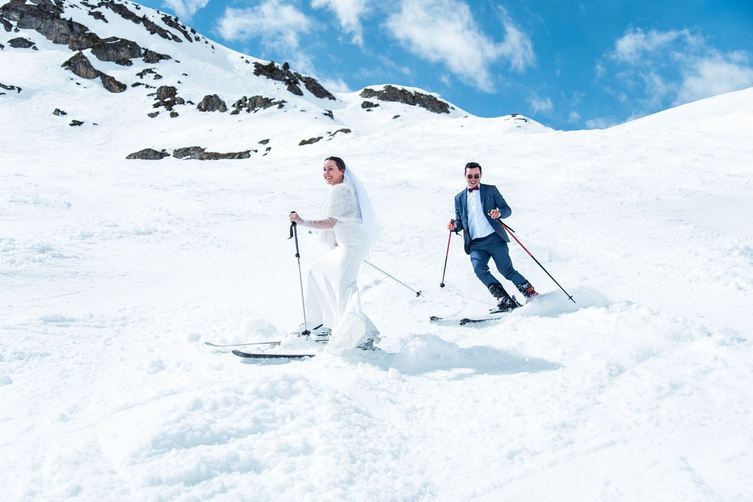 Skiers glide down a snow-covered mountain slope against a bright blue sky on a sunny winter day.