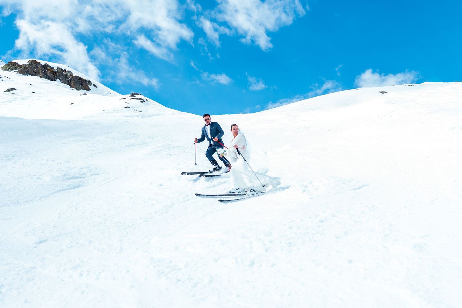 Skier gliding down a snowy mountain slope against bright blue sky and white snow conditions.