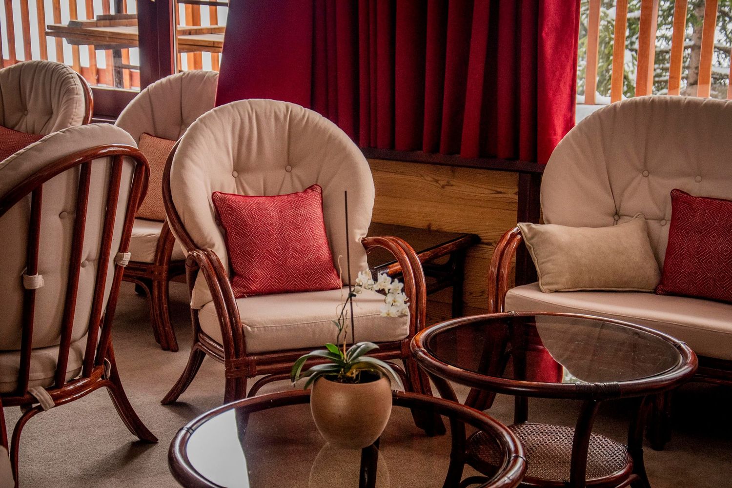 Cozy indoor seating area with beige armchairs, red accent pillows, wooden trim, and round glass coffee tables.