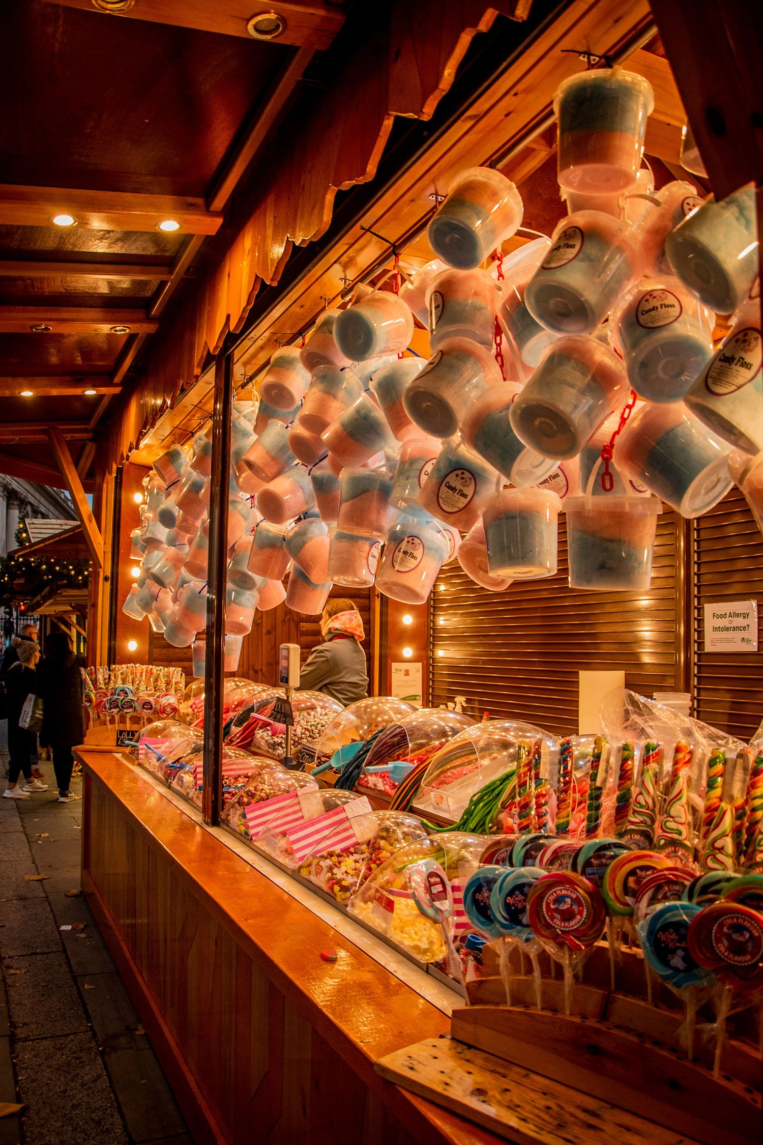 Illuminated festival market stall displaying colorful candy and treats with glowing lanterns overhead at night.