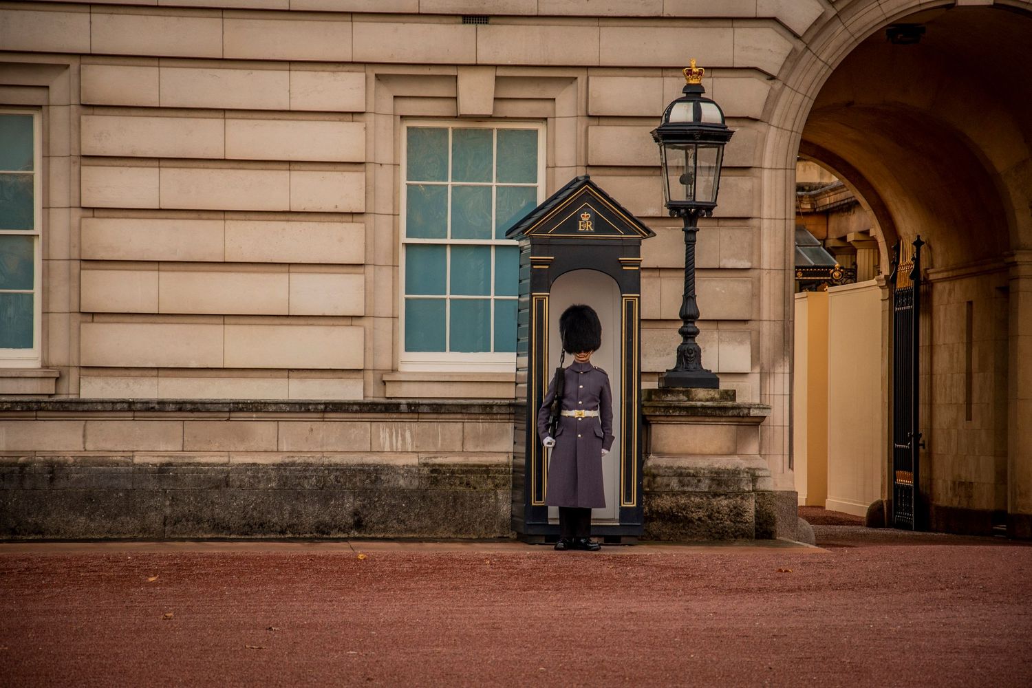 A guard stands at attention in traditional uniform outside Buckingham Palace in London behind a sentry box.
