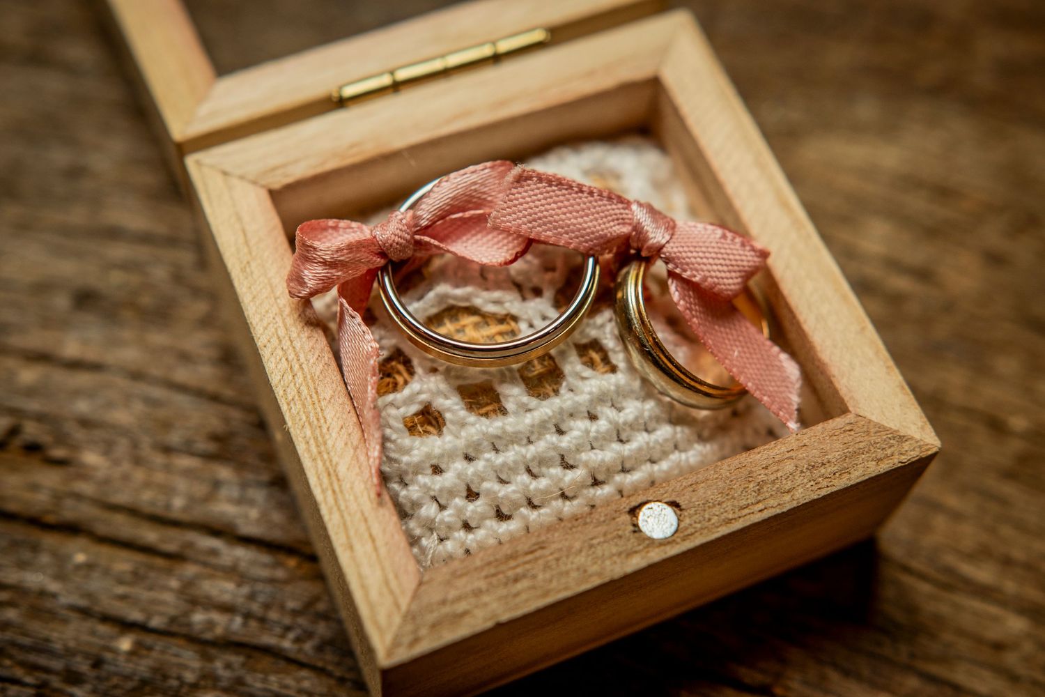 A wooden ring box with lace detail opens to reveal a diamond wedding ring on rustic wood surface.