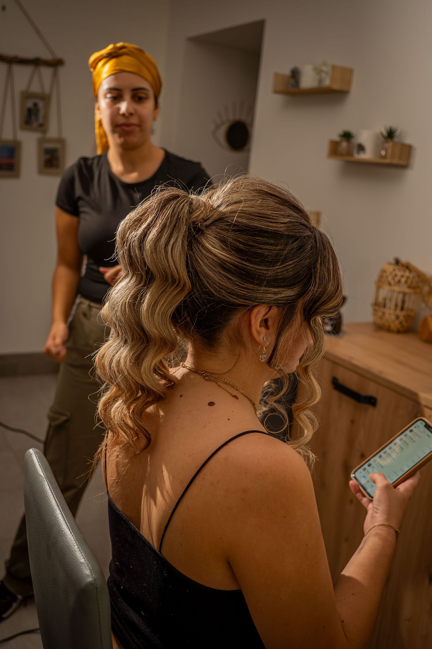 Person with brown hair tied up looks at a mobile phone while seated in a dimly lit room.