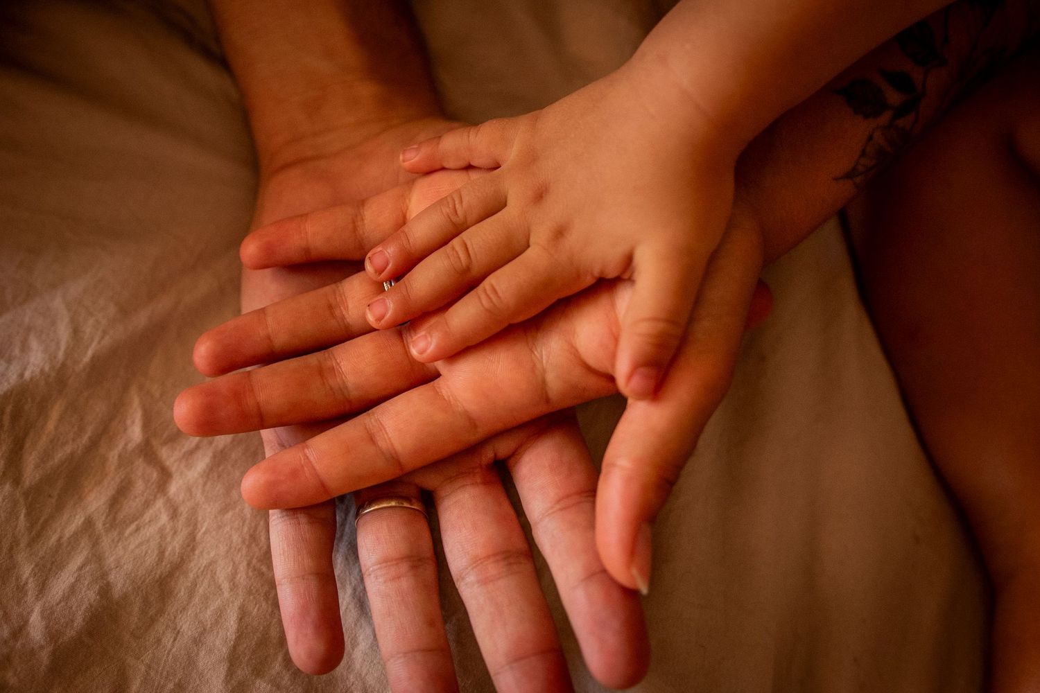 Three hands of different sizes lovingly placed on top of each other against a soft beige fabric background.