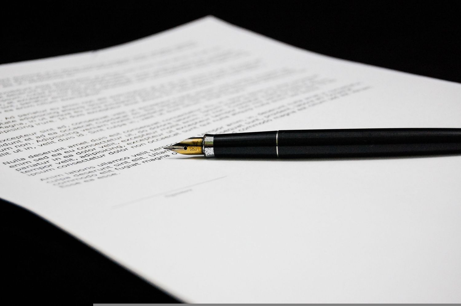 An elegant fountain pen rests on white business documents showing contract signing and legal paperwork.