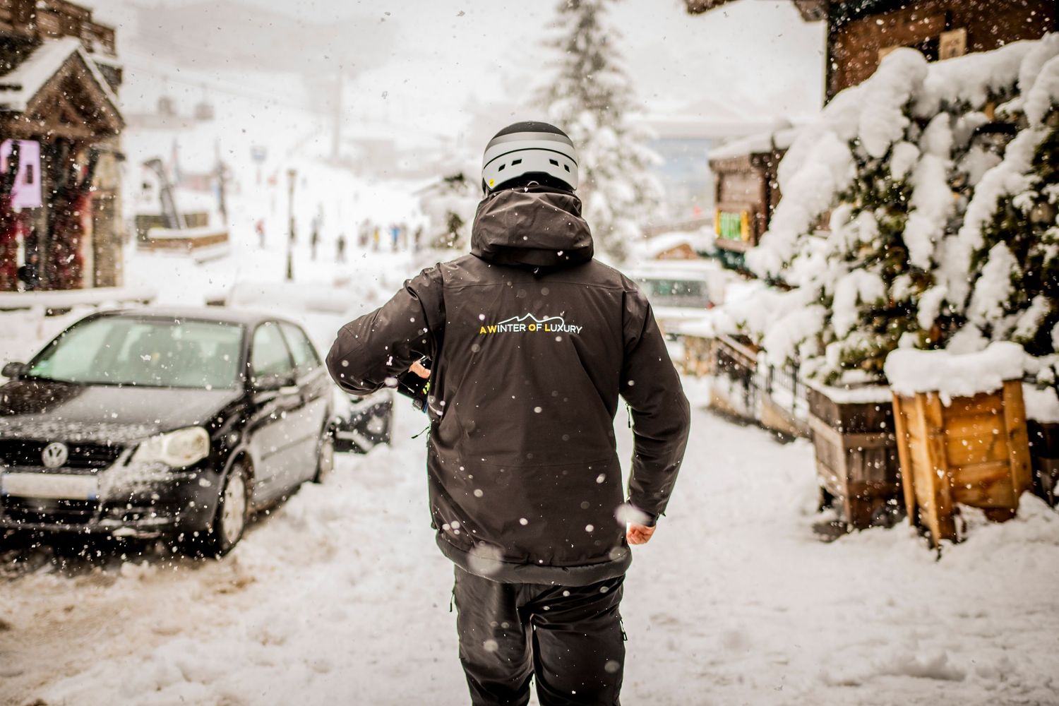 Rear view of someone with a motorcycle helmet walking on a snowy street in a winter resort village.