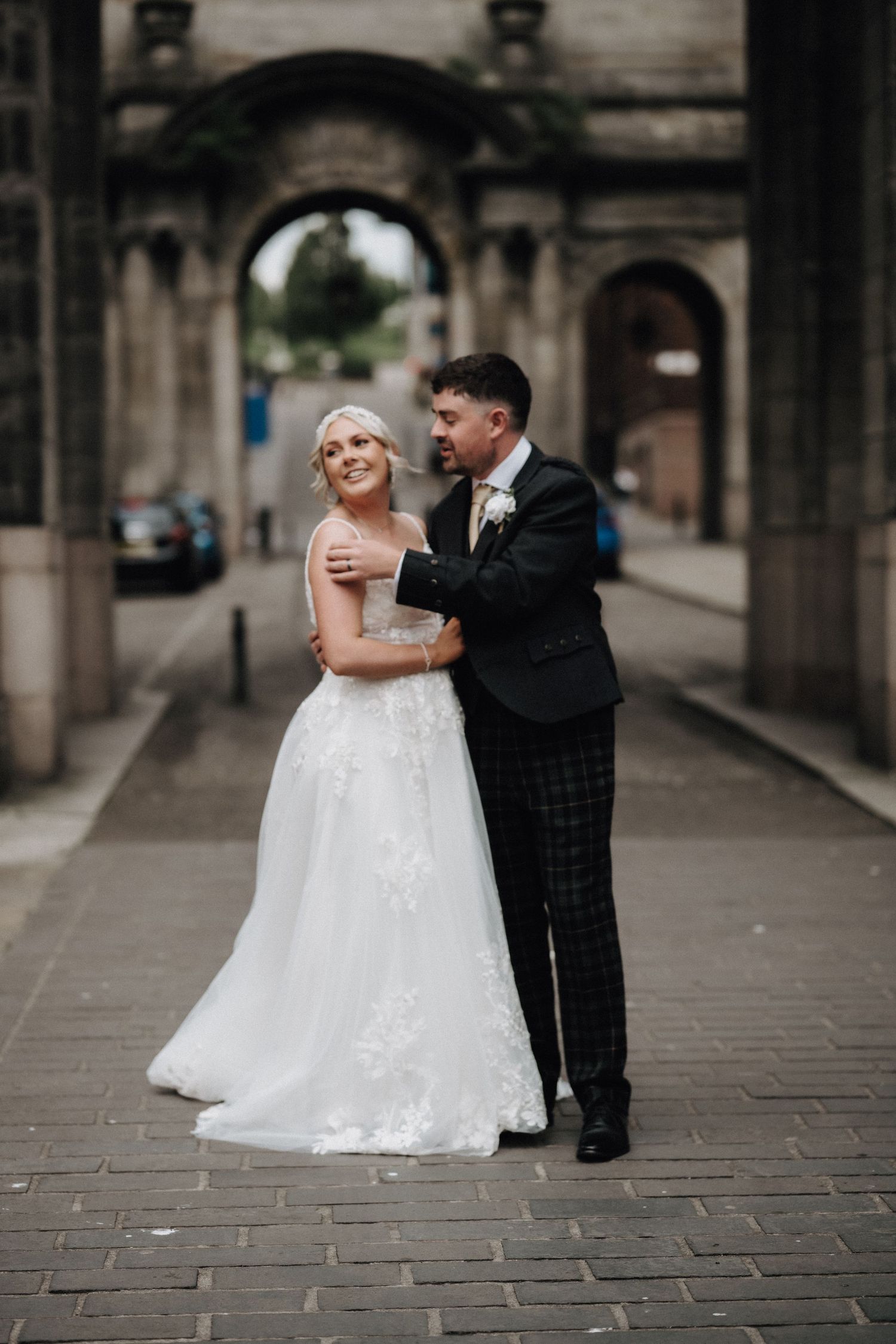 Newlyweds sharing a joyful moment under an ornate stone archway.