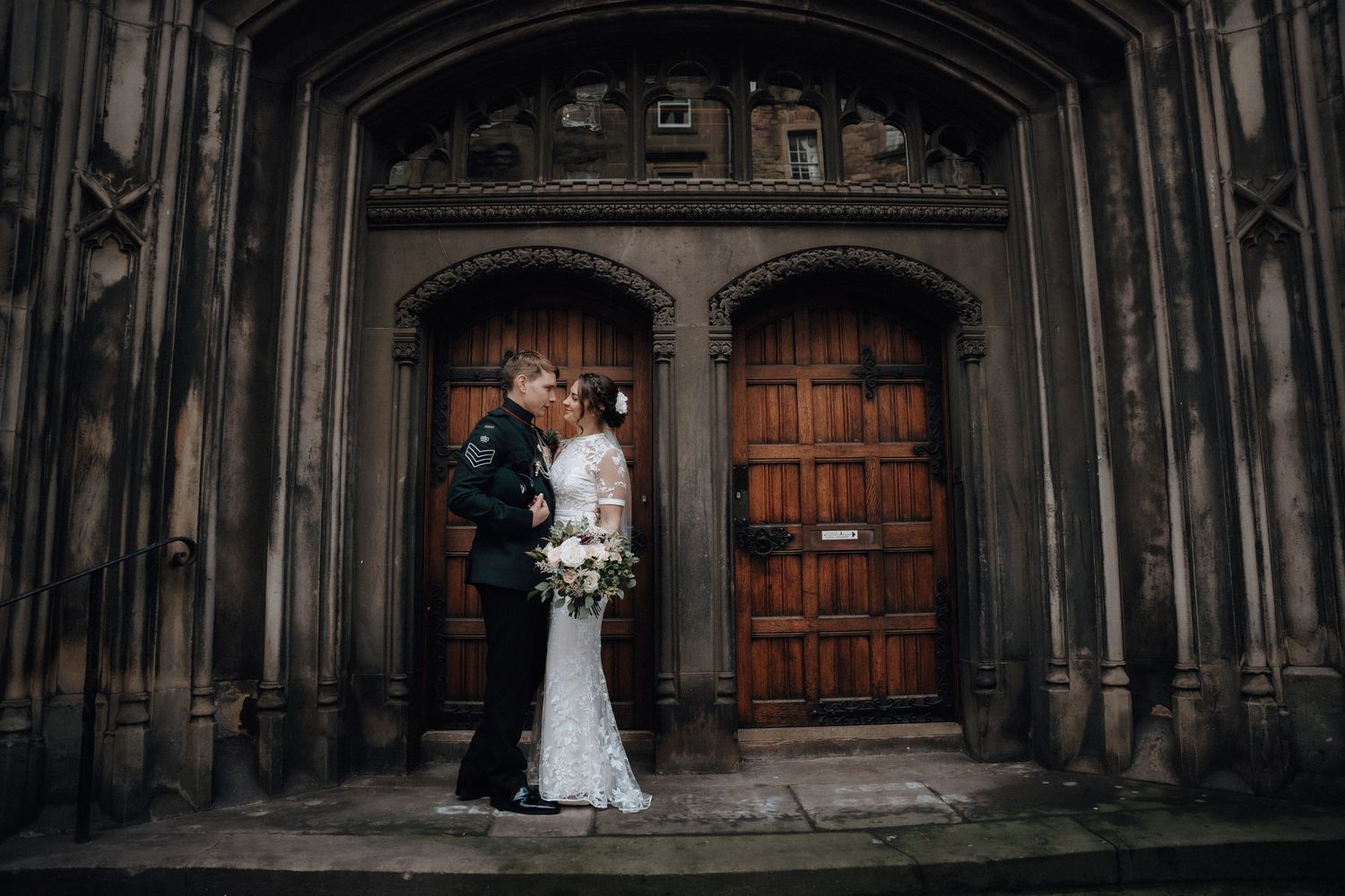 Wedding couple poses in front of gothic wooden doors and stone archway.