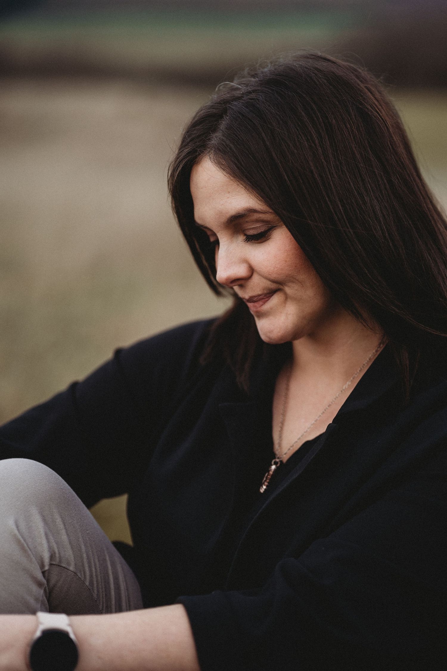 A candid portrait of someone in black clothing sitting outdoors with a gentle smile.