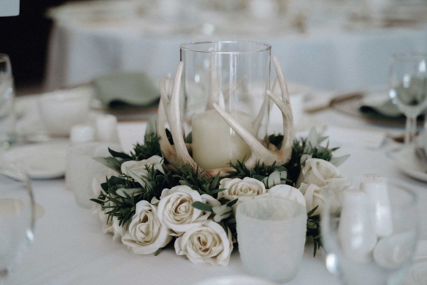 Elegant wedding table centerpiece with white roses and candles in glass holders.