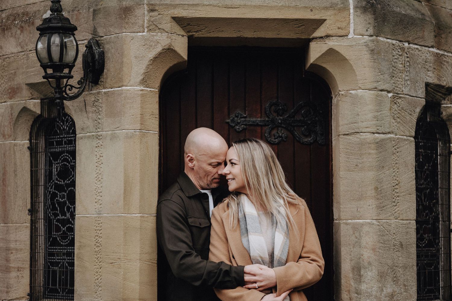 A couple embraces intimately in front of a historic stone doorway with gothic architecture.