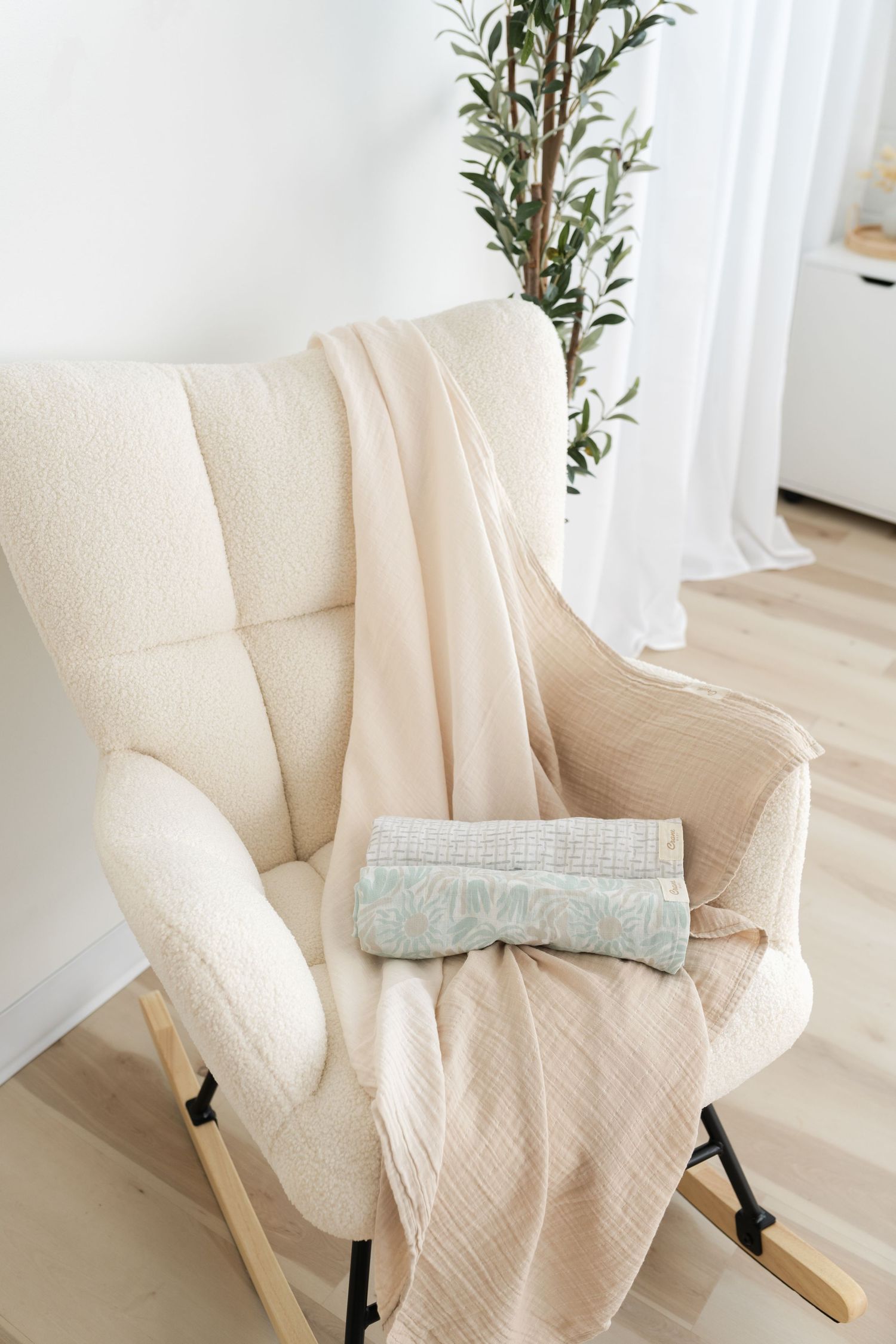 A cozy cream-colored rocking chair with folded blankets in a minimalist nursery setting.