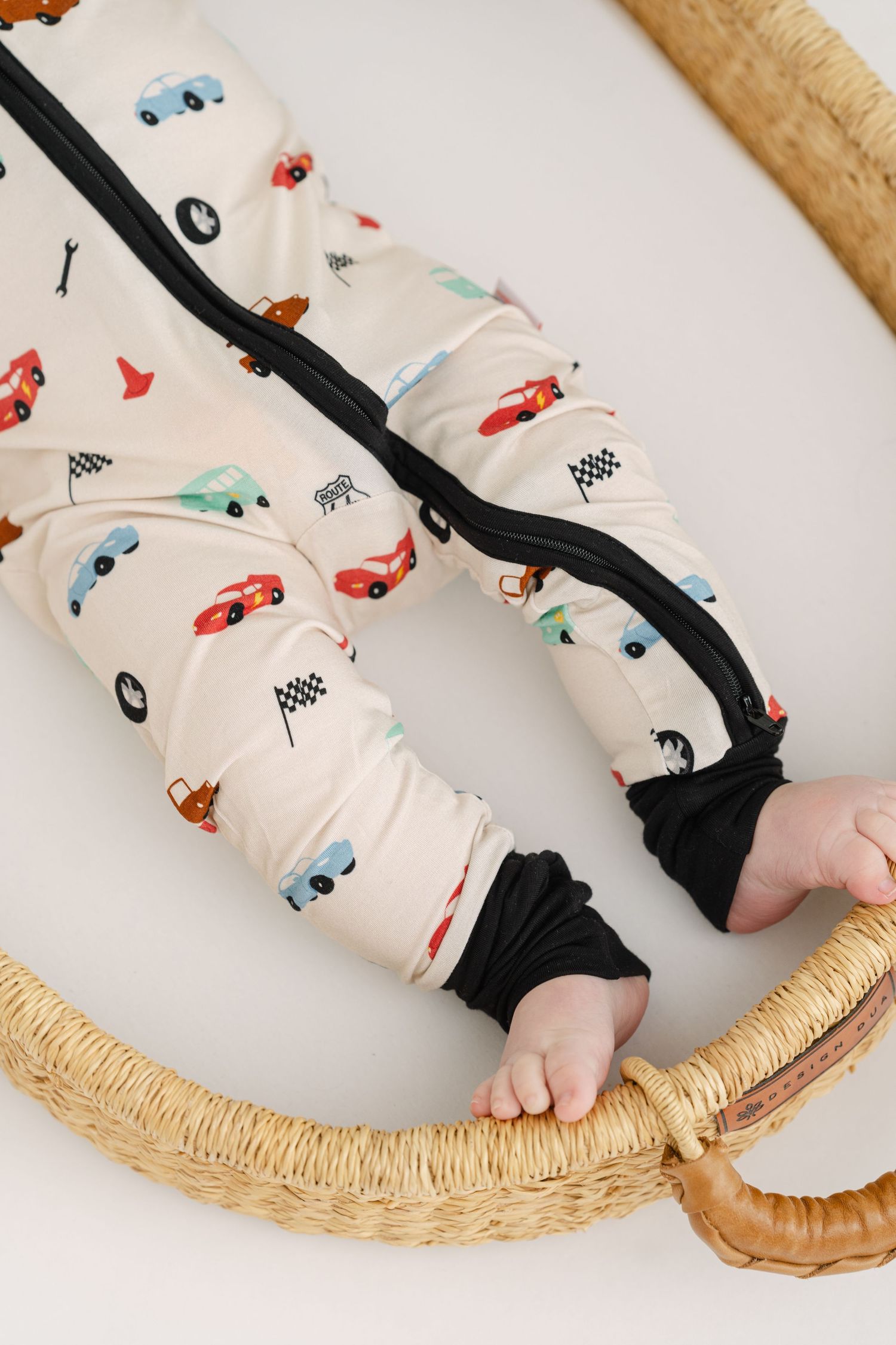Whimsical baby pants with car print design and black stripes on a rattan chair.