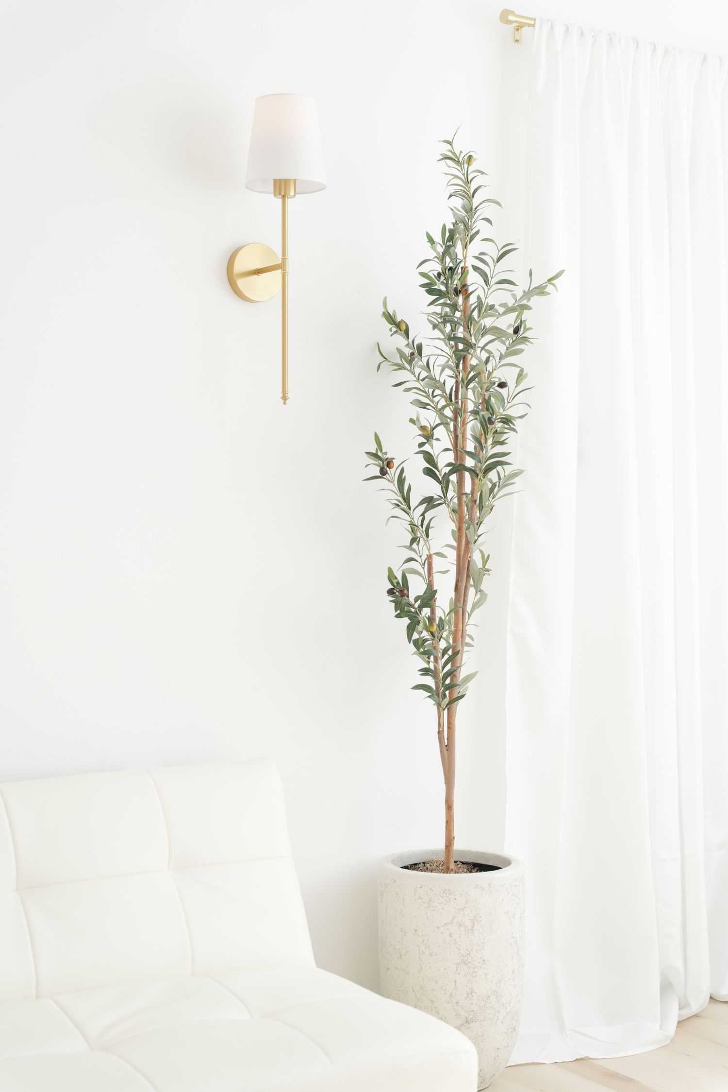 Modern white room with gold wall sconce and tall plant in concrete planter.
