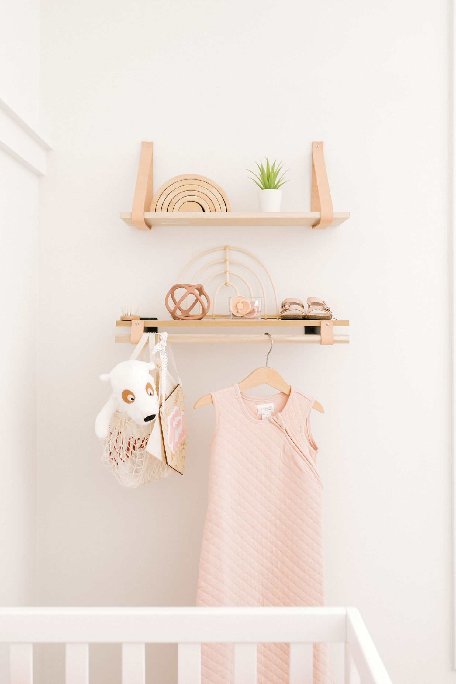 Minimalist nursery shelves with natural decor and pink dress hanging.