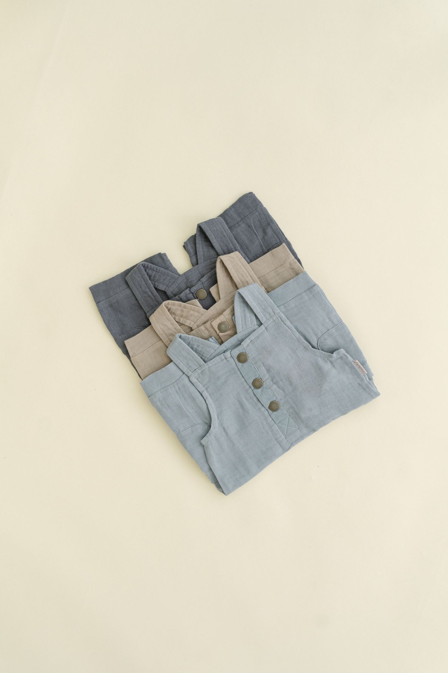 Folded blue and beige baby overalls arranged on a neutral background.