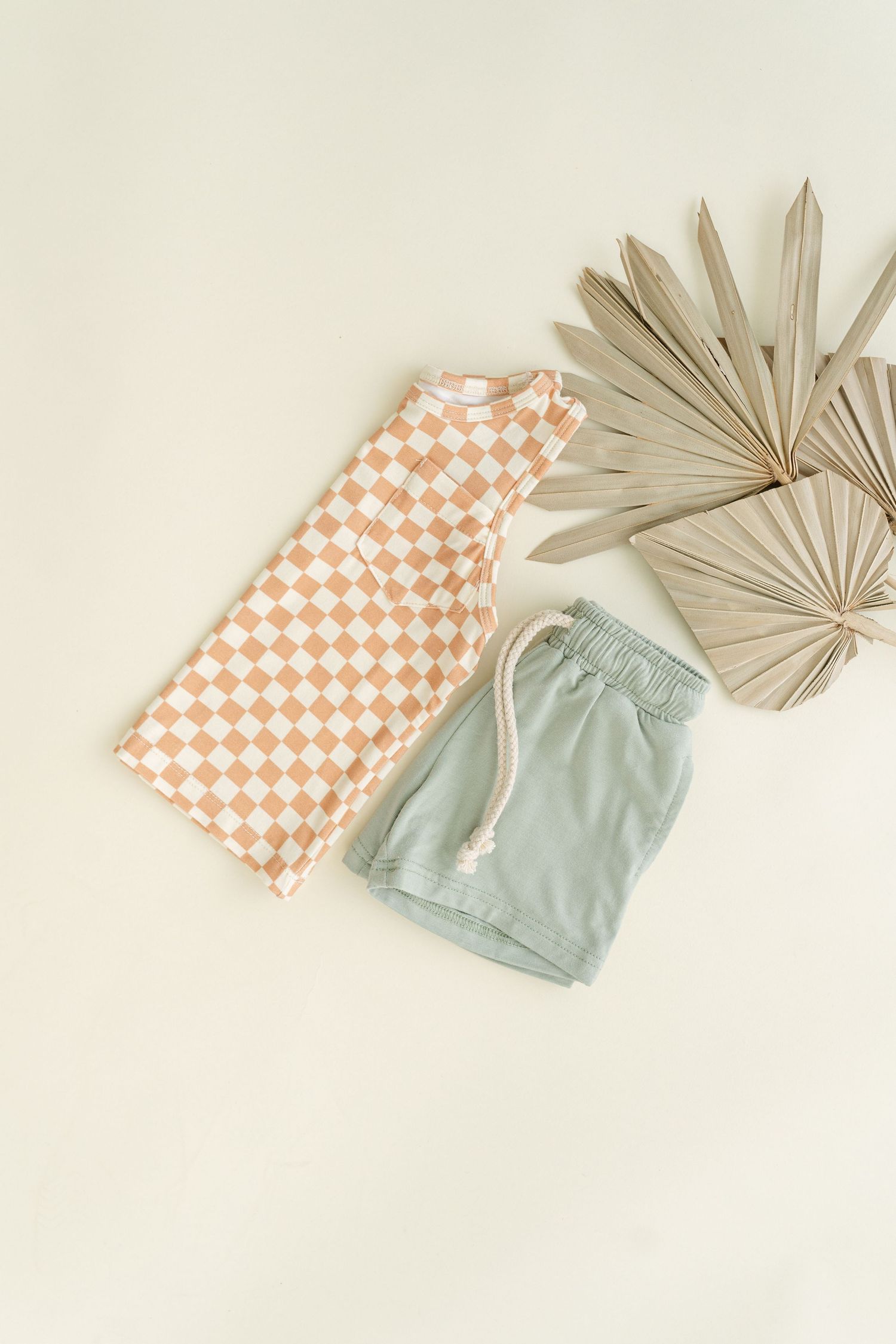 Orange checkered shirt and mint green shorts with dried palm leaves on beige background.