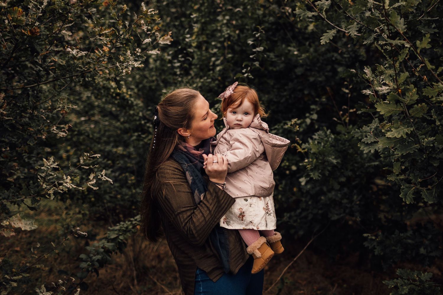 Parent and child share a tender moment together outdoors surrounded by green foliage on an autumn day.