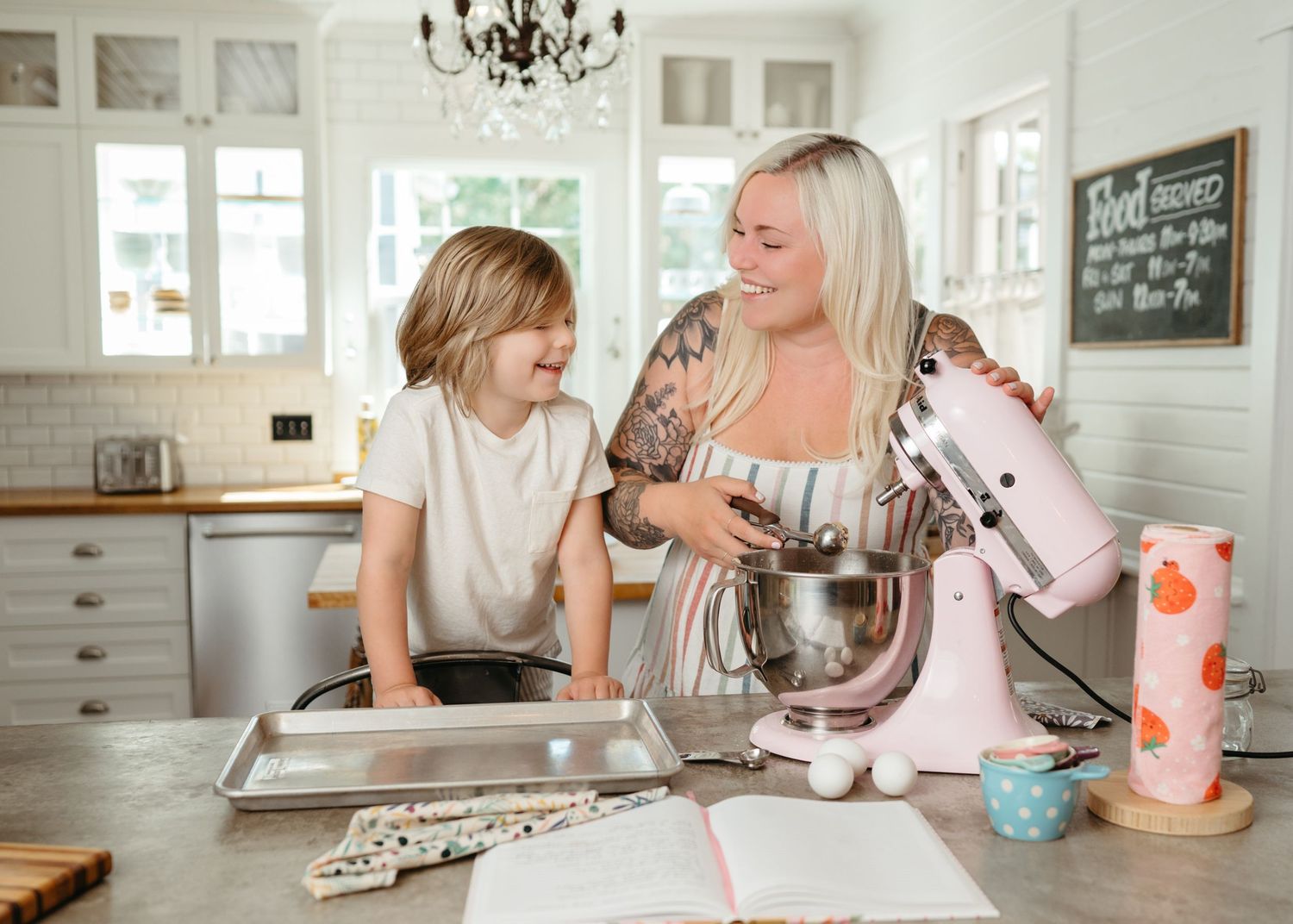 Two people enjoying a baking session together in a bright modern kitchen with a stand mixer and cookbook.