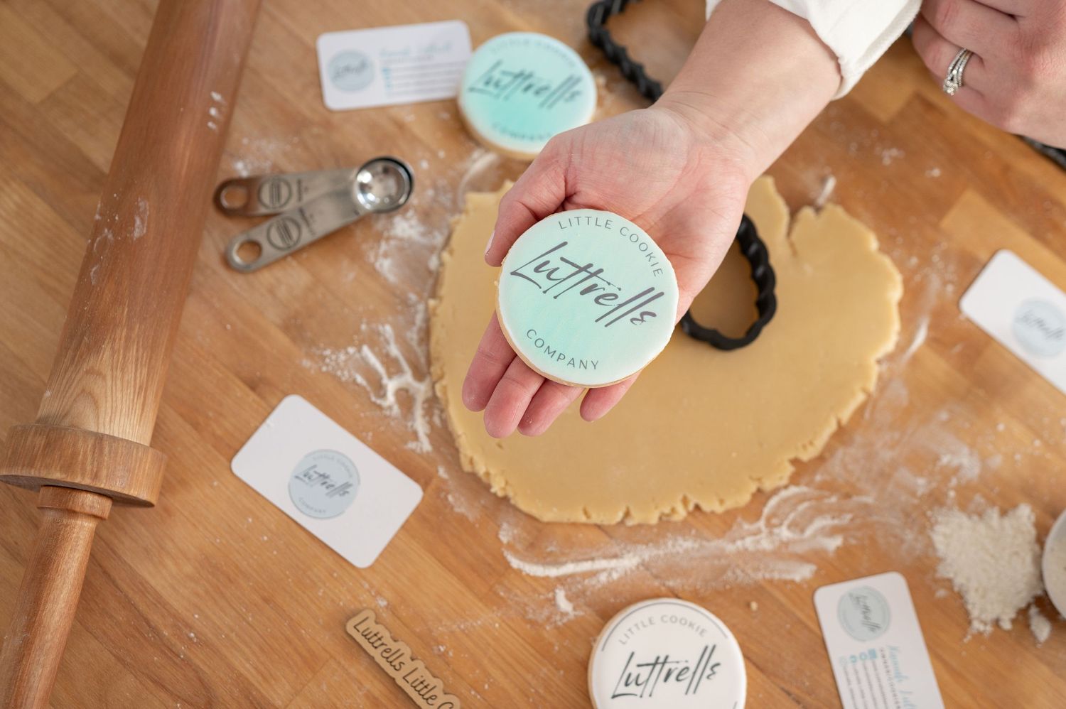 Hands rolling out dough with mint colored cookie cutters and baking supplies.