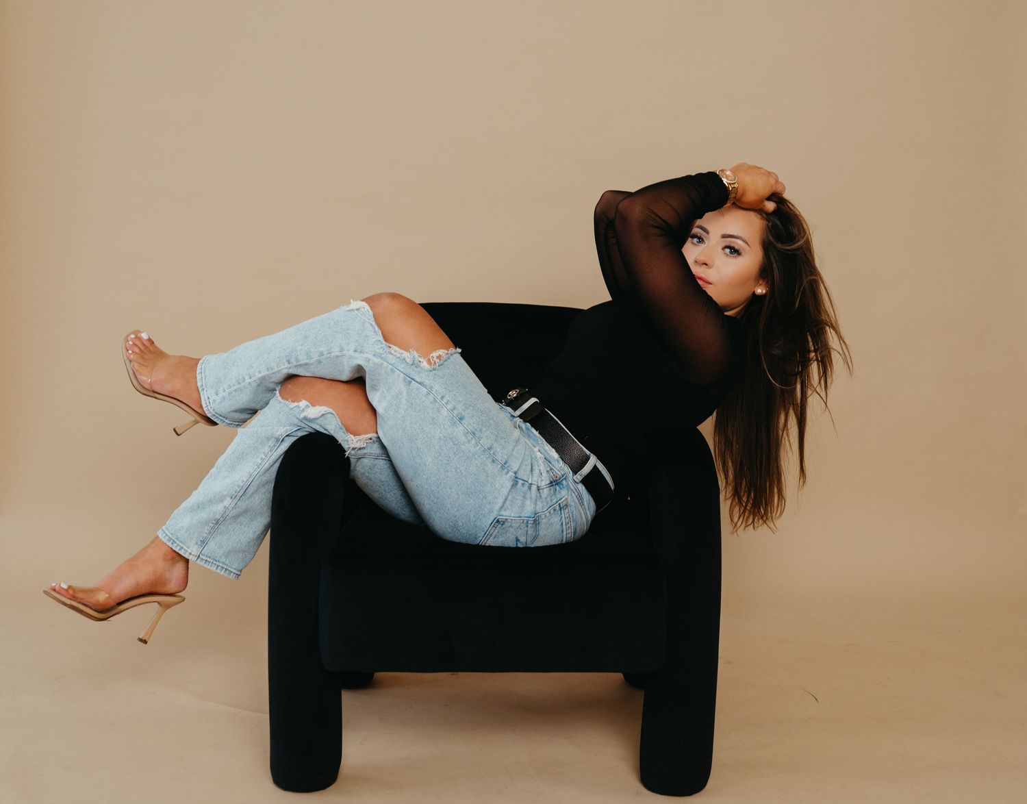 Lifestyle portrait on black chair wearing distressed jeans and black sweater.
