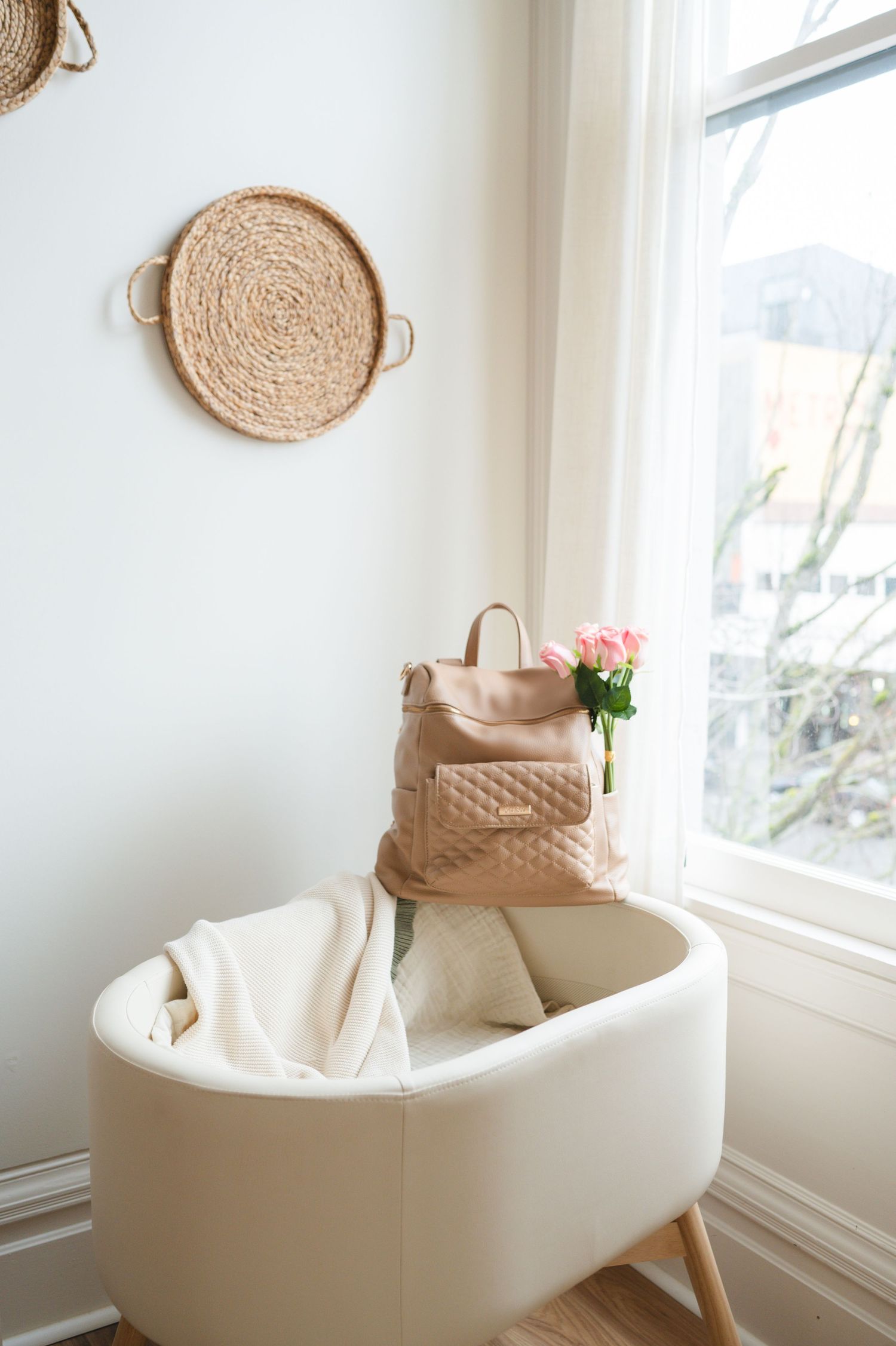 Modern minimalist corner nook with white curved chair, woven wall decor, handbag and pink roses by bright window.