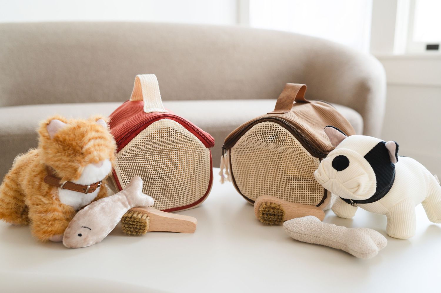Cute plush stuffed animals including a ginger cat, mouse, and black and white dog arranged around small shoes on beige couch.