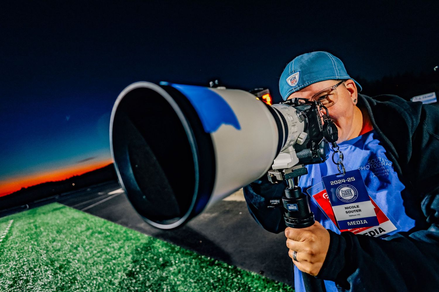 Sports photographer using professional telephoto lens equipment on field.