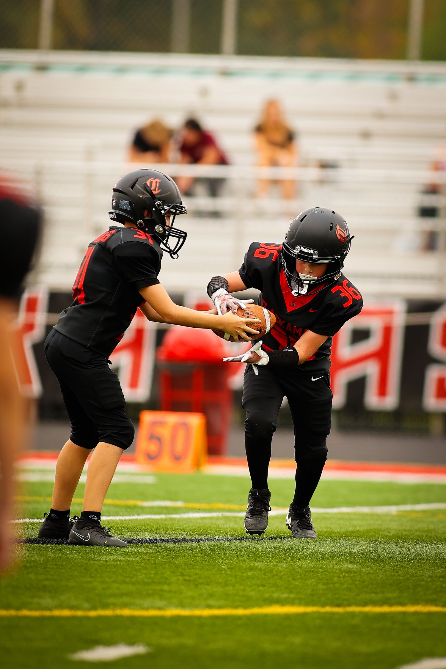 Four football players stretch and warm up on a field before a game in black and red uniforms.