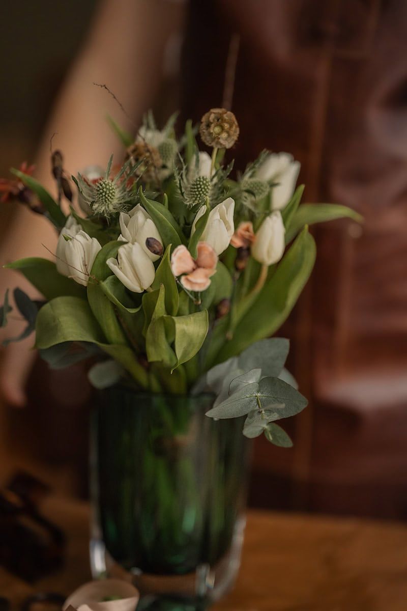 White tulips and green foliage arranged in a dark green glass vase.