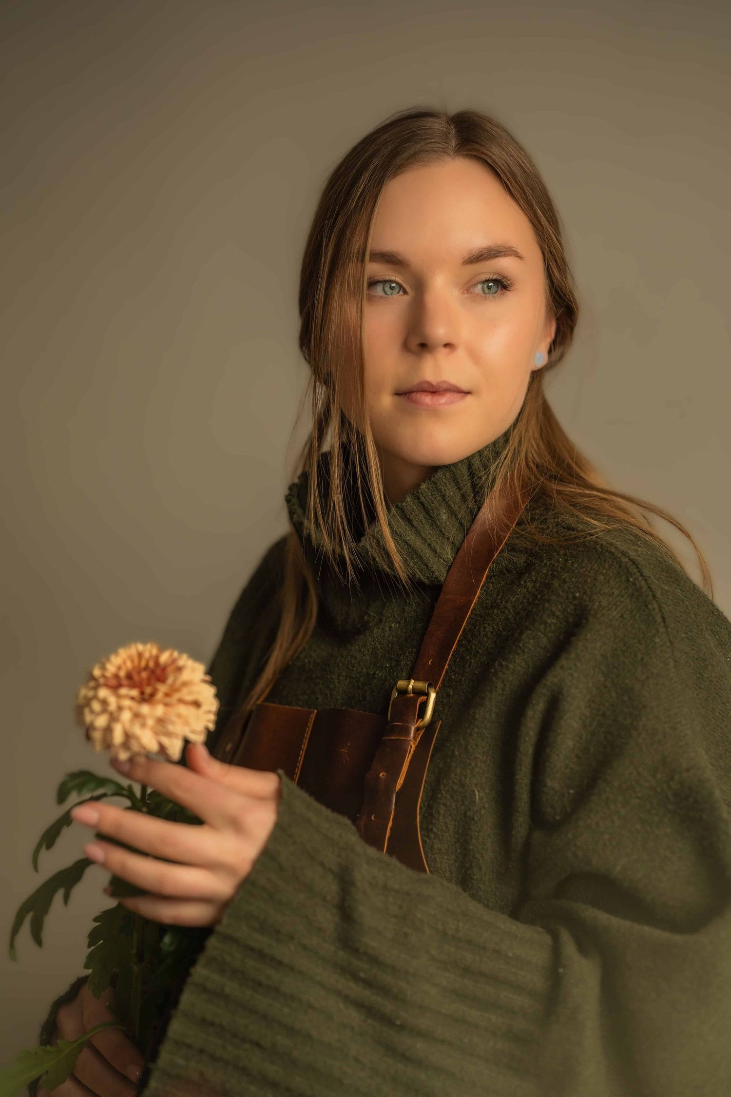 A person in a green sweater and brown apron holds a fresh flower in soft lighting.