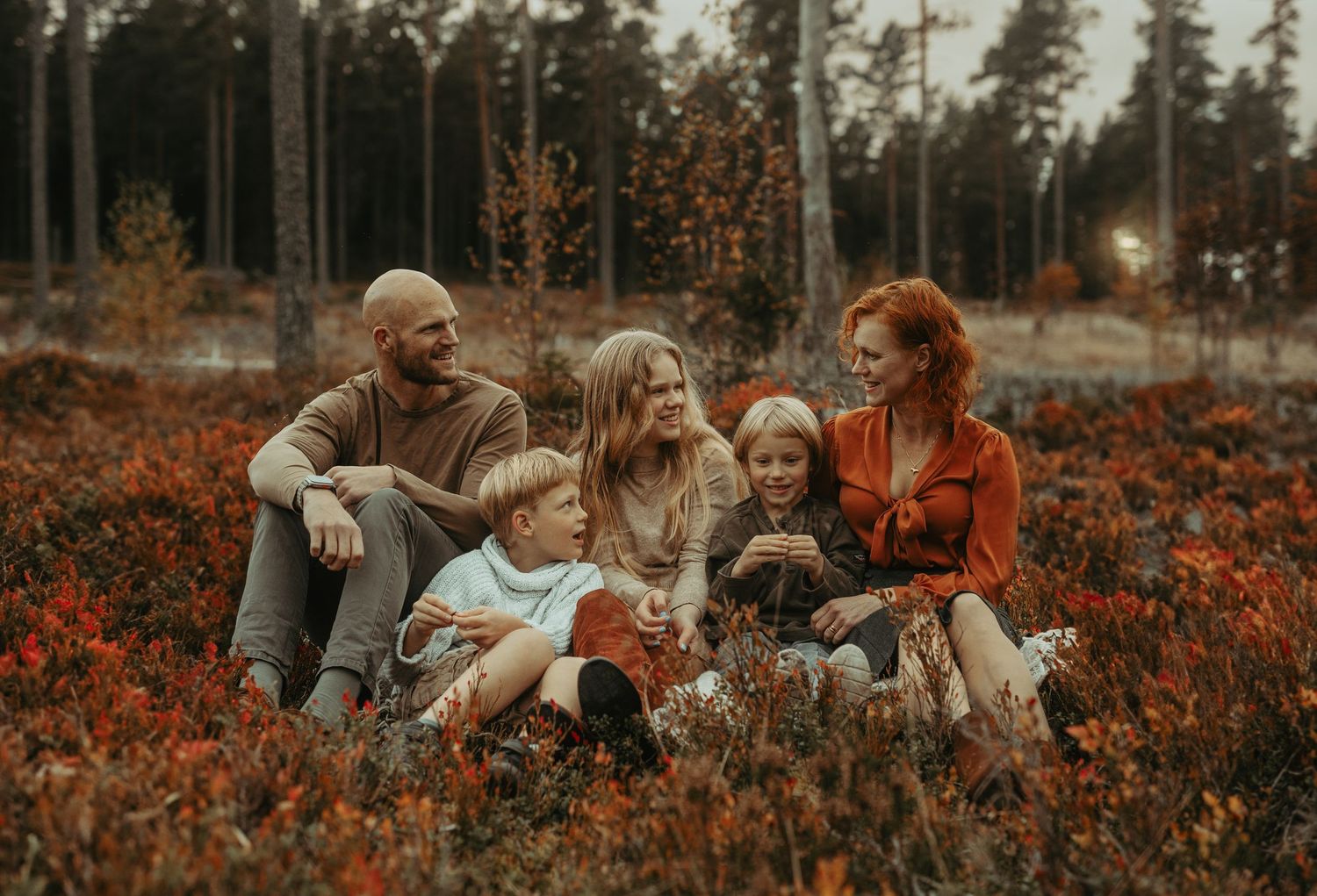 Family sitting together in a vibrant orange wildflower field during golden hour at sunset, creating a warm autumn scene.