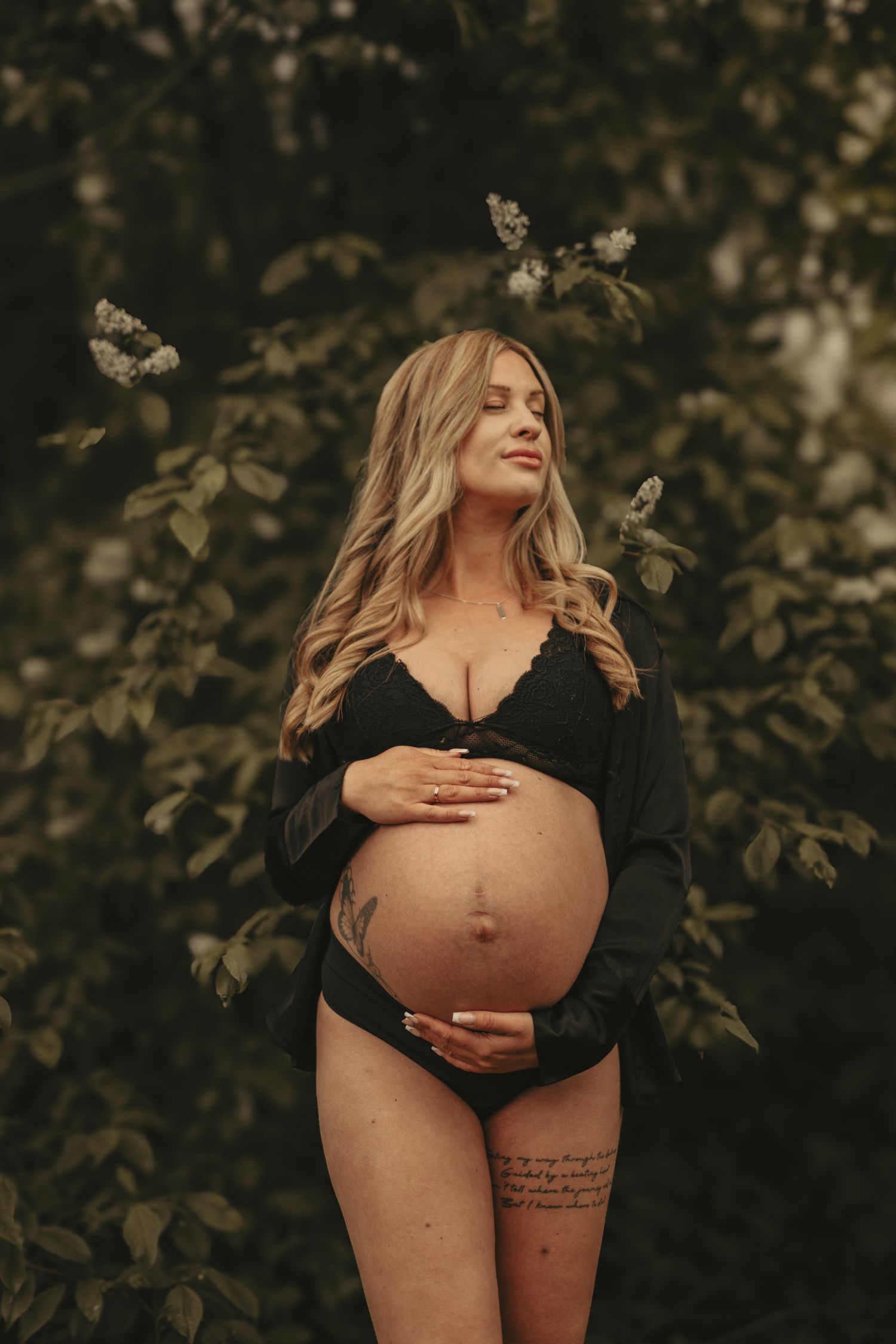 A maternity photoshoot captures intimate moments of an expectant mother in dark clothing against a natural outdoor backdrop.